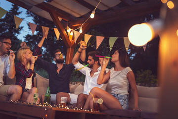 Friends having fun at an outdoor party, blowing party whistles