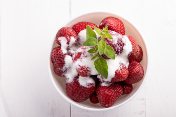 strawberries in a white bowl with cream and leaves of lemon balm on white background