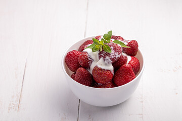 strawberries in a white bowl with cream and leaves of lemon balm on white background
