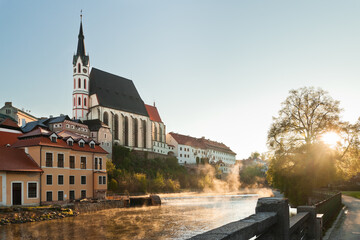 Obraz premium Cesky Krumlov and it St. Vitus church at an early morning golden hour from the riverbank of Vltava river during lockdown