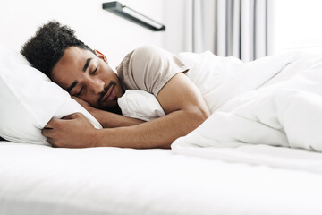 Photo of young african american man with mustache sleeping in white bed
