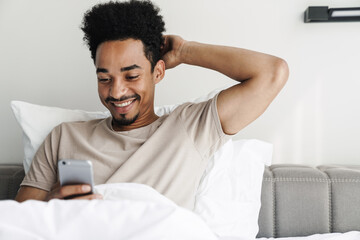 Photo of happy african american man using mobile phone and smiling