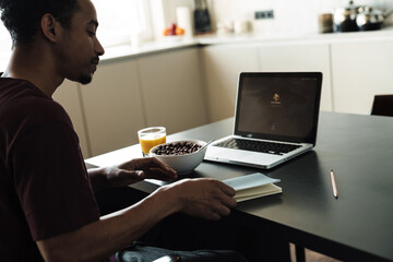 Photo of african american man working with laptop while having breakfast
