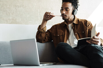 Photo of african american man using headphones while working with laptop
