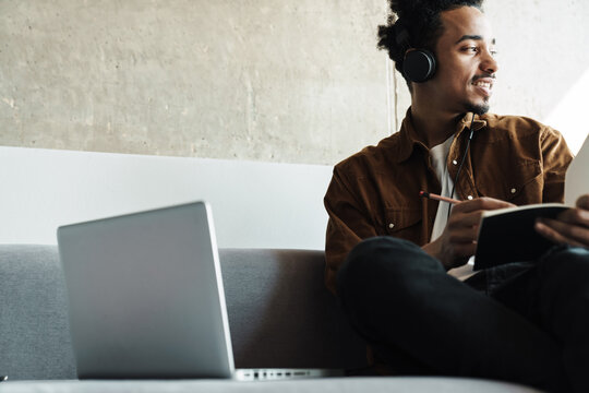 Photo of african american man using headphones while working with laptop