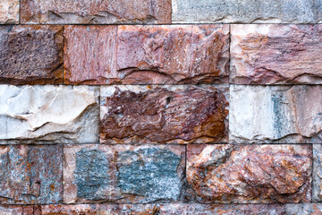 The wall is made of textured marble of different colors. A stone wall with an interesting marble texture. The marble facing of the wall.