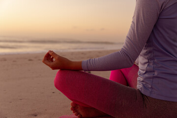 Mid section of woman performing yoga on the beach during sunset