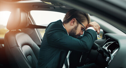 Exhausted businessman resting or sleeping on steering wheel staying in car somewhere in countryside