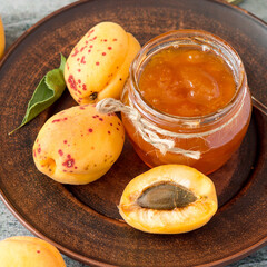 Glass jar with homemade fruit jam and fresh apricots on a round ceramic plate. Selective focus.