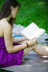 young woman sitting on blanket in park and reading a book
