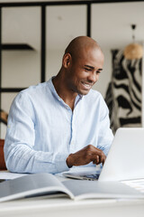 Photo of african american man working with laptop while sitting at table
