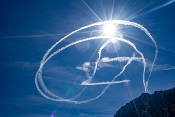 Fighter jet contrails chemtrails blue sky with sun in background 