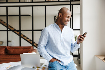 Photo of laughing african american man using mobile phone while working