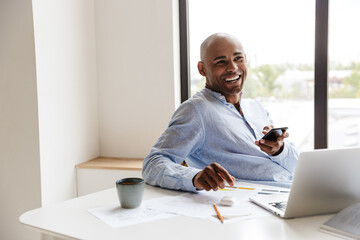 Photo of african american man using cellphone while working with laptop