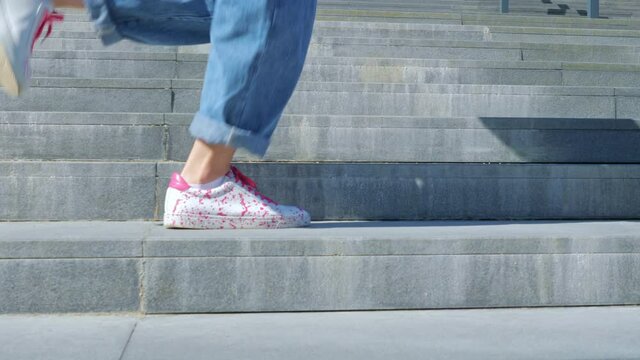 A happy teenage girl is dancing a shuffle on the stairs and enjoying life next to a modern building. The concept of carefree, youth culture and city life