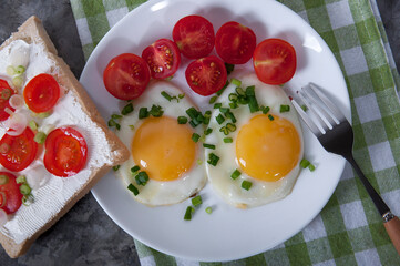 An appetizing breakfast with fried eggs, bread, cherry tomatoes and cheese. Fried eggs for breakfast. Sandwich with cheese and cherry tomatoes.