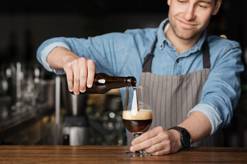 Fototapeta na wymiar Repeat the order. Bartender in apron and denim shirt, pours dark beer in glass