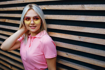blonde in sunglasses against the background of wooden boards looks to the top