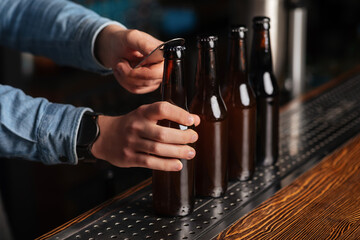 Fototapeta na wymiar Bartender opens lot of glass bottles with lager on wooden bar counter