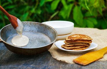 cooking pancakes in a frying pan on the background of greenery in nature in a rustic style