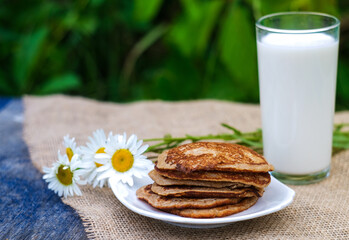 pancakes daisies and milk on a background of greenery in nature in a rustic style on a linen canvas fabric