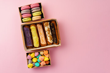 Carton boxes with eclair cakes and cookies on pink surface