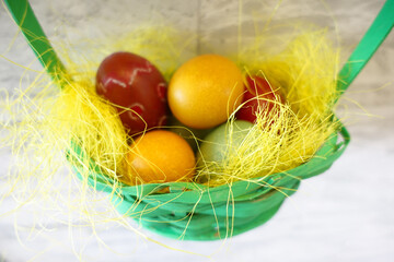 Colorful painted eggs in yellow nest in green basket close up. Happy easter!