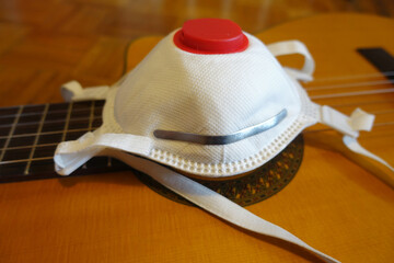 Medicine mask with vent on guitar body, close up. Concept of quarantine during corona virus time.