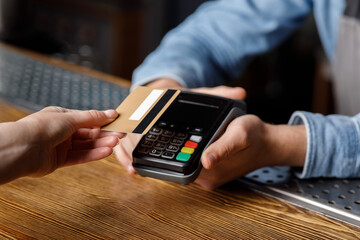 Client pays for drinks at bar. Barman holds terminal, female hand puts credit card