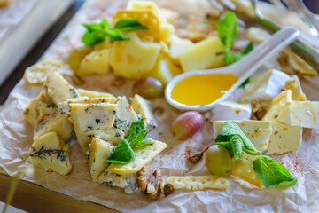 Cheese plate decorated with fresh mint leaves, close-up. Delicious appetizers of different types of cheese served with honey, cracker and grapes. Perfect accompaniment to wine.