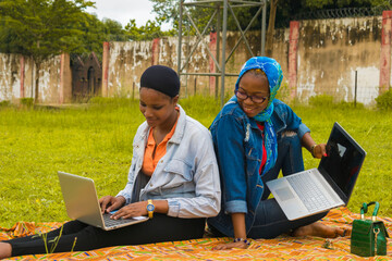 young beautiful black ladies sitting outside, using their laptops and catching fun