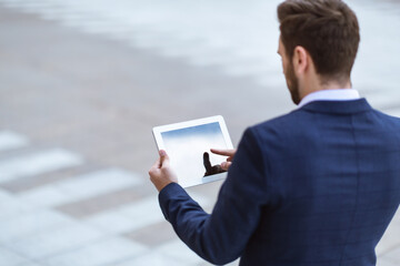 Back view of office executive holding tablet with blank screen in city centre, space for your text...