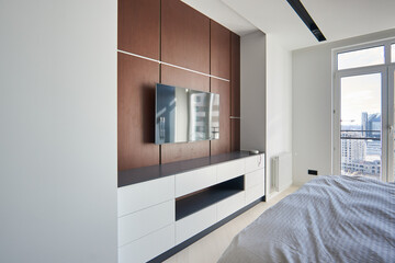 A modern bedroom with a TV area and a double bed with a soft headboard and a walnut veneer wall above it