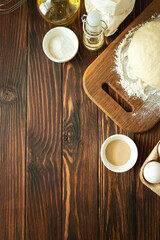 Fototapeta na wymiar Baking in rural kitchen. Dough and recipe ingredients on vintage brown wooden table. Top view. Rustic background