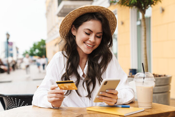 Portrait of young laughing woman using cellphone and holding credit card