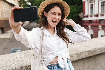 Portrait of cheerful woman winking and taking selfie on cellphone