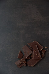 Dark chocolate stack, chips and cocoa powder on a dark background. Confectionery and food concept. Top view, copy space, selective focus.