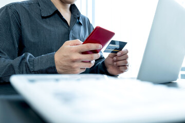 The businessman's hand is holding a credit card and using a smartphone for online shopping and internet payment in the office