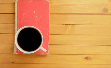 Top view, A cup of coffee and closed red book on wooden background