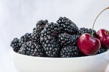 Blackberries and double cherry stalk on a white bowl in front of the white background, close up, macro photography