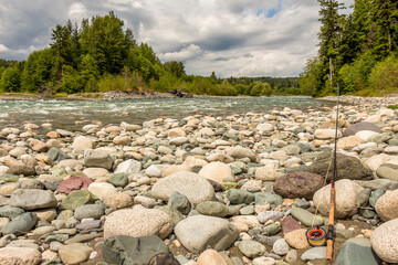 Fly rod resting on boulders beside a fast flowing river in British Columbia, Canada.