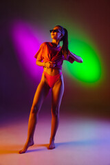 Fototapeta na wymiar Seductive young girl' portrait isolated on bicolored neon studio background in neon. Fit sportive woman in bodysuit. Facial expression, summer, weekend, beauty, resort concept. Vacations.