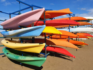 Multi-colored canoes ( kayaks ) are stacked in a row on the beach.