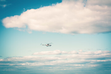 The helicopter is flying in the sky. Bright sunny day. Blue sky with clouds.