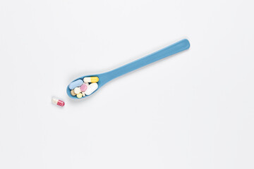 medicine, healthcare and pharmacy concept - blue spoon with different colored pills on a white background. Copy space