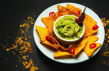 Guacamole e pimenta vermelha com nachos em fundo preto