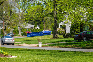 A long blue dumpster in the driveway of a house on a residential street that is being renovated