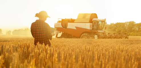 Woman farmer with digital tablet on a background of harvester. Smart farming concept.