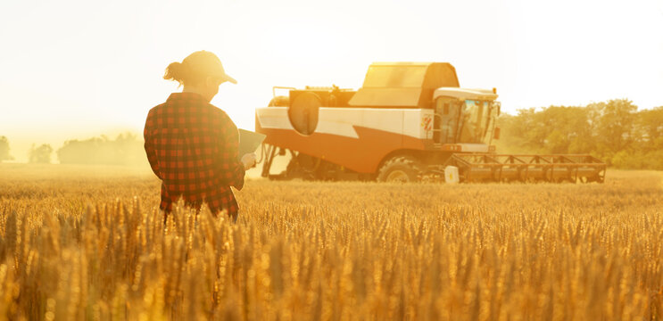 Woman Farmer With Digital Tablet On A Background Of Harvester. Smart Farming Concept.