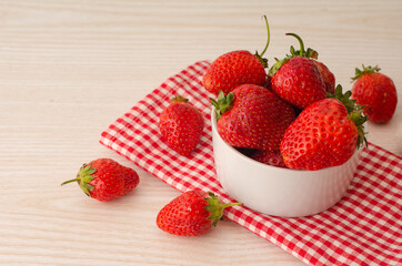 Fresh red strawberries in a white bowl on light background and towel